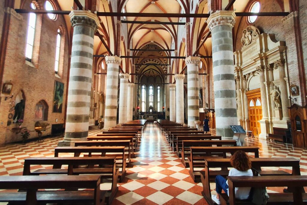 Der weite Innenraum der Kirche San Lorenzo mit markanten, gestreiften Säulen, hölzernen Kirchenbänken und hohen Gewölbedecken.