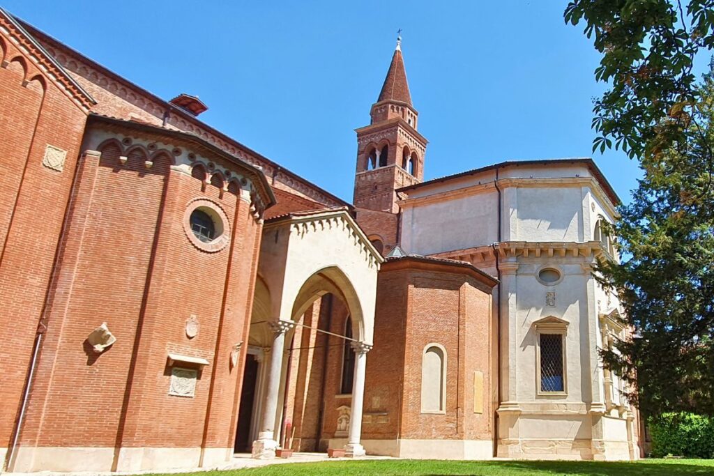 Die Außenansicht der gotischen Kirche Santa Corona in Vicenza mit rotem Mauerwerk, hellen Steinelementen und einem spitzen Glockenturm unter blauem Himmel.
