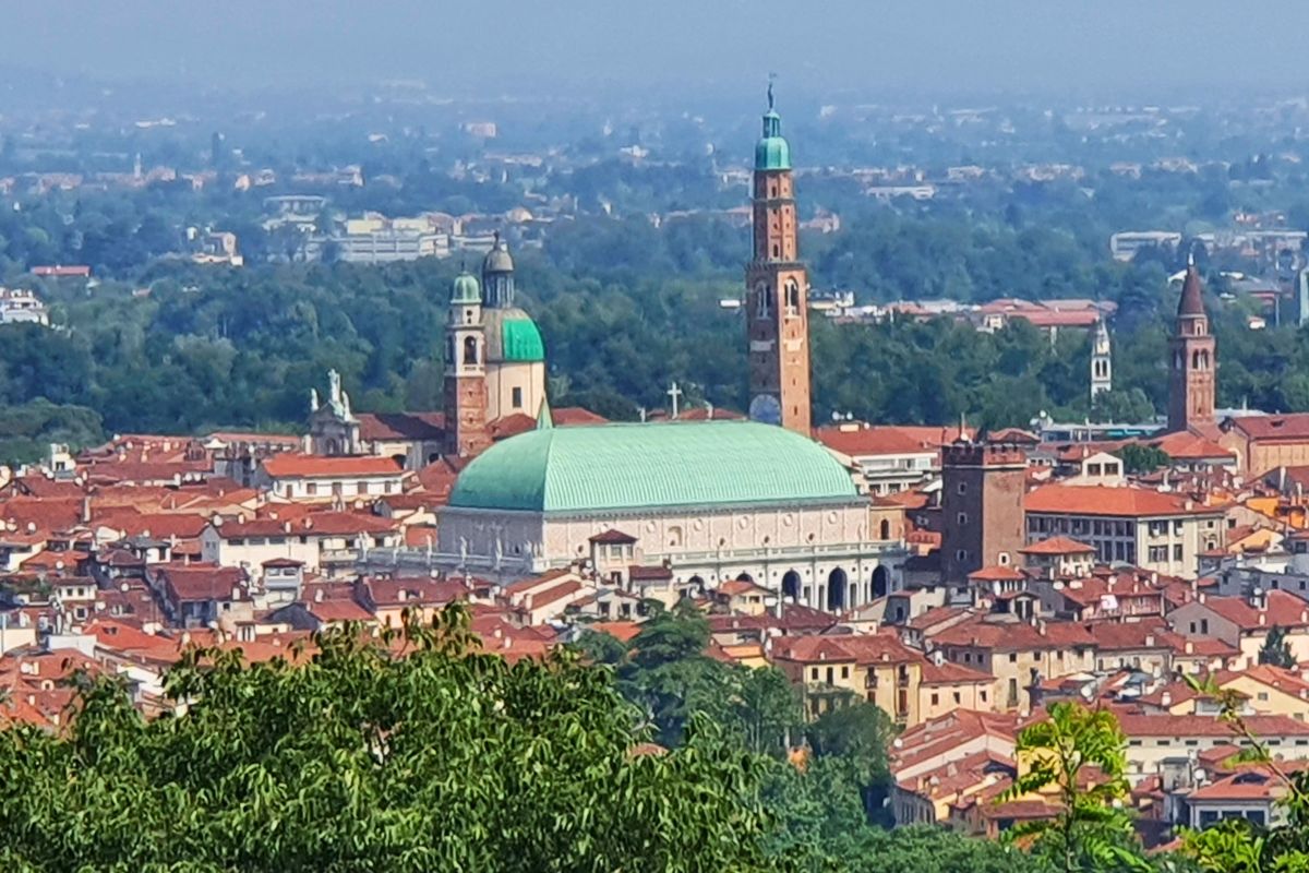 Panorama-Ansicht über die roten Dächer von Vicenza. Im Zentrum stechen das leuchtend grüne Dach der Basilica Palladiana und der hohe Torre Bissara hervor.