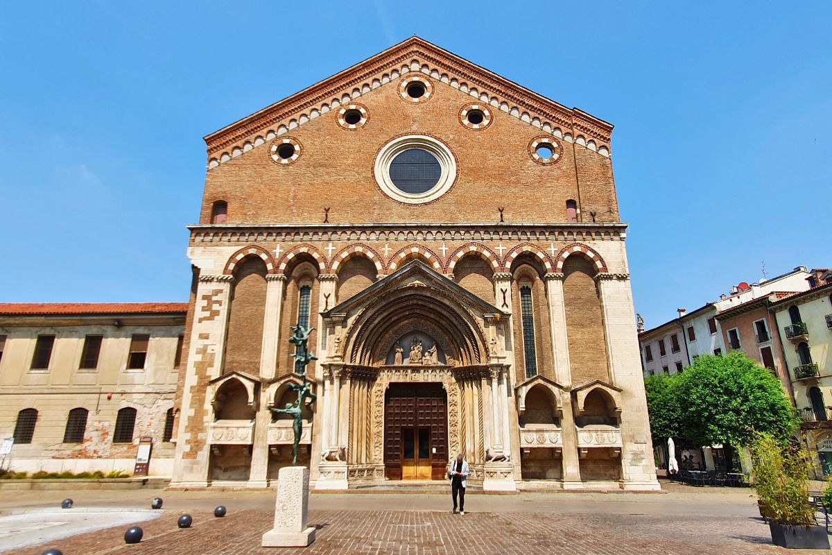 Die imposante Backsteinfassade der Kirche San Lorenzo in Vicenza mit einem großen, detailreichen gotischen Portal und einem runden Rosenfenster unter strahlend blauem Himmel.