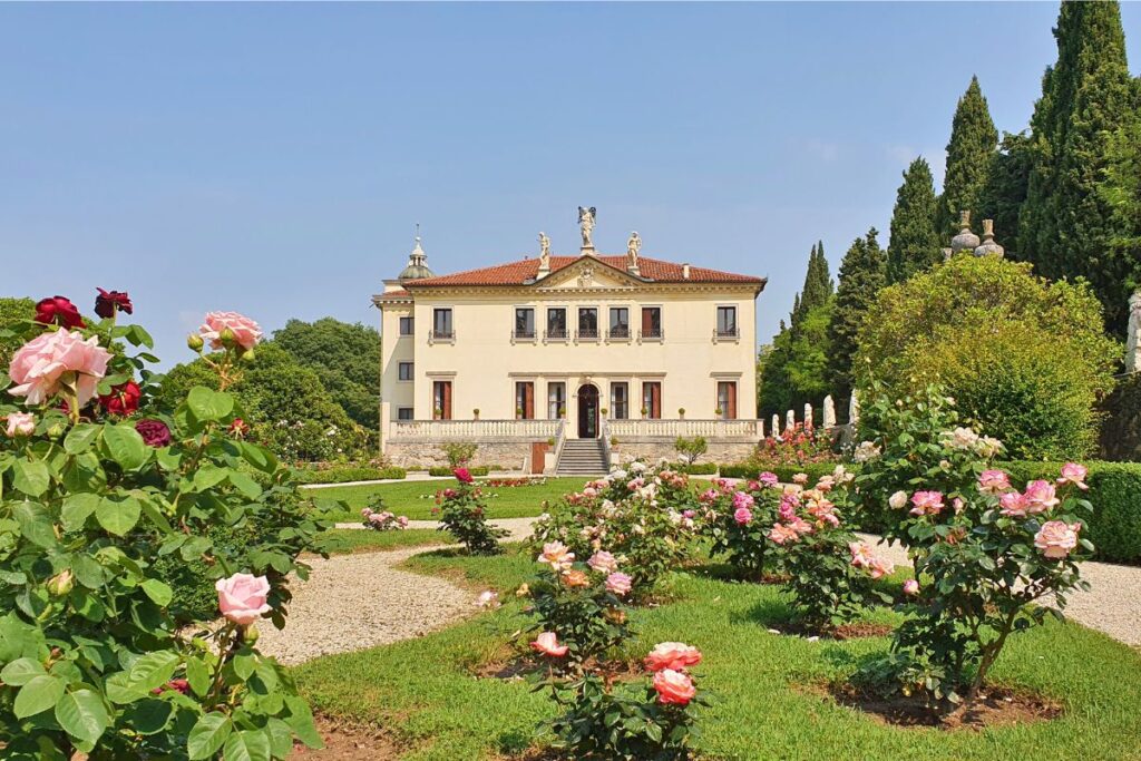 Die helle Fassade der Villa Valmarana ai Nani in Vicenza, davor ein blühender Rosengarten unter strahlend blauem Himmel.