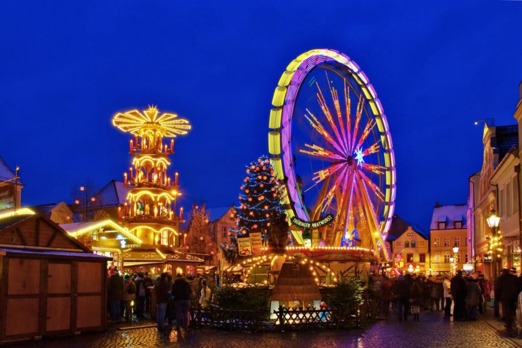 Der beleuchtete Weihnachtsmarkt in Cottbus bei Nacht mit einem großen Riesenrad, einer Weihnachtspyramide und festlichen Buden auf dem Altmarkt