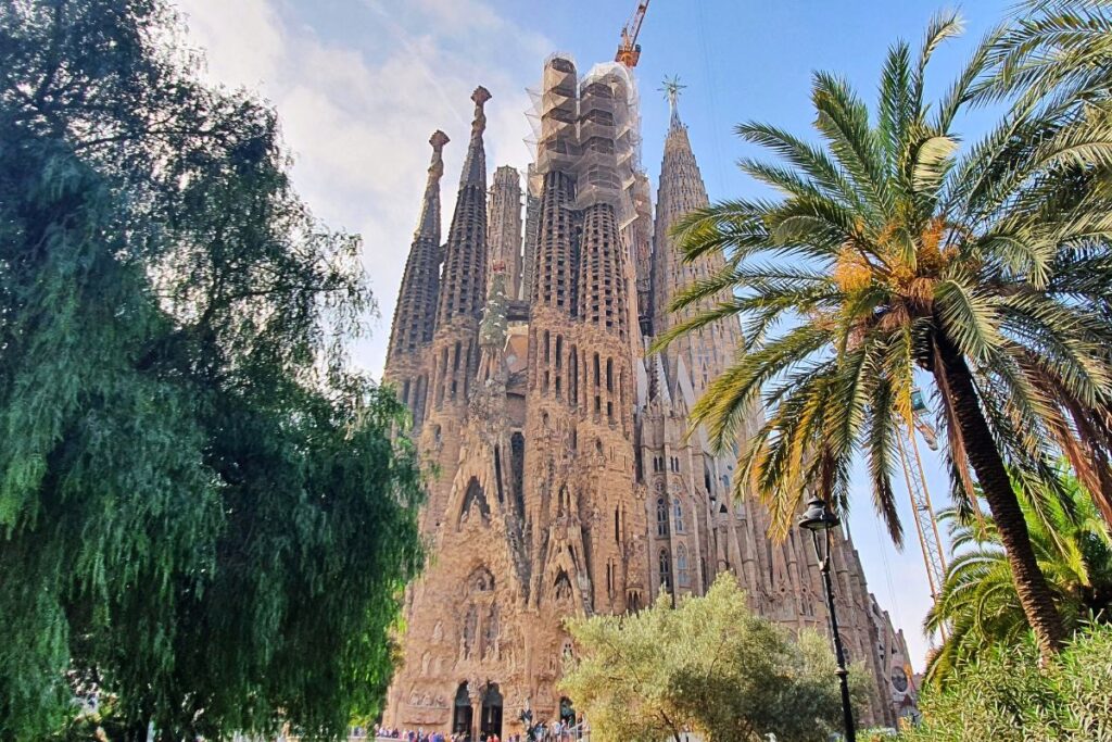 Die imposante Basilika Sagrada Família in Barcelona hinter grünen Palmen unter einem hellblauen Himmel.
