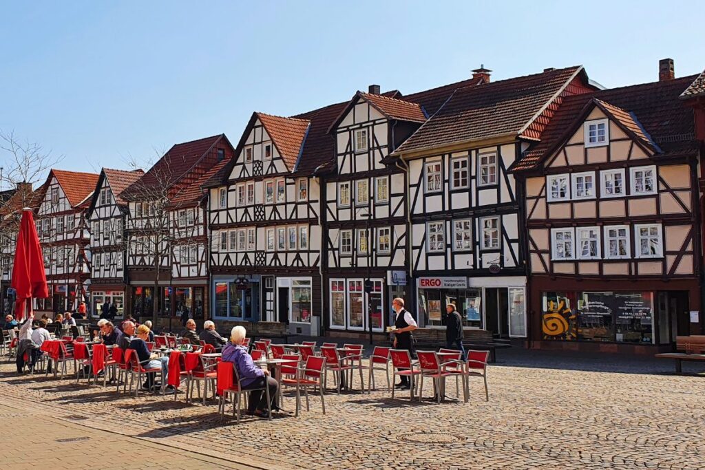 Eine belebte Gasse in der Altstadt von Eschwege mit Außengastronomie, roten Sonnenschirmen und einer geschlossenen Reihe prachtvoller Fachwerkhäuser.