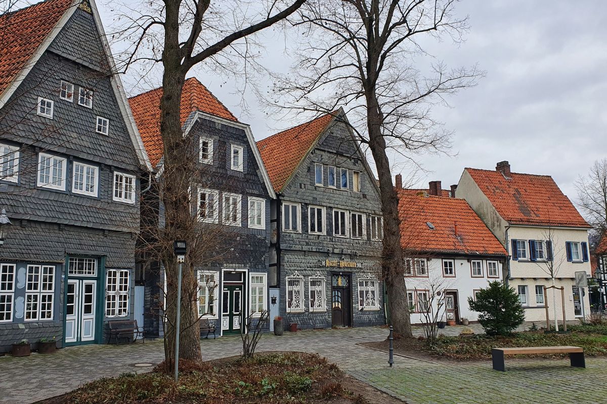 Eine Reihe historischer Fachwerkhäuser und schieferverkleideter Gebäude am Alten Kirchplatz in Gütersloh unter bewölktem Himmel.