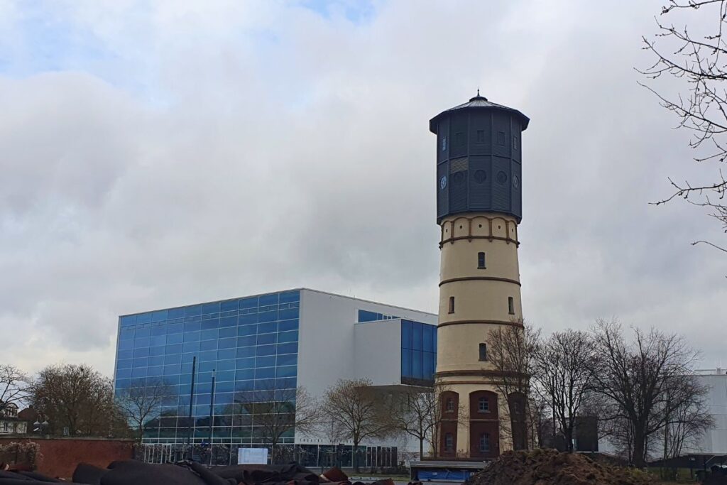 Der historische Gütersloher Wasserturm steht direkt neben der modernen, bläulichen Glasfassade des Theaters Gütersloh.