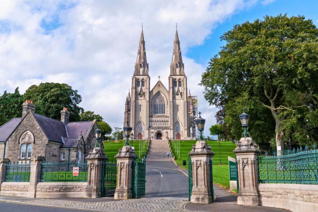 Blick durch ein steinernes Tor auf die imposante St. Patrick’s Cathedral in Armagh, die auf einem grünen Hügel thront.