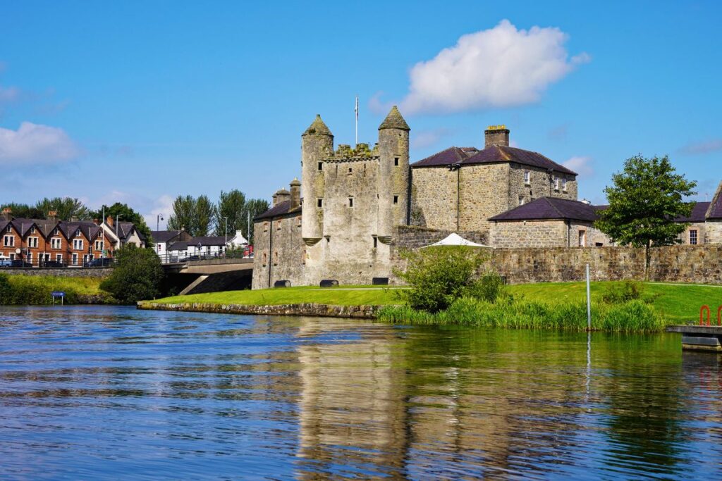 Das historische Enniskillen Castle aus massivem Stein spiegelt sich im blauen Wasser des Flusses Erne unter einem weiten Sommerhimmel.