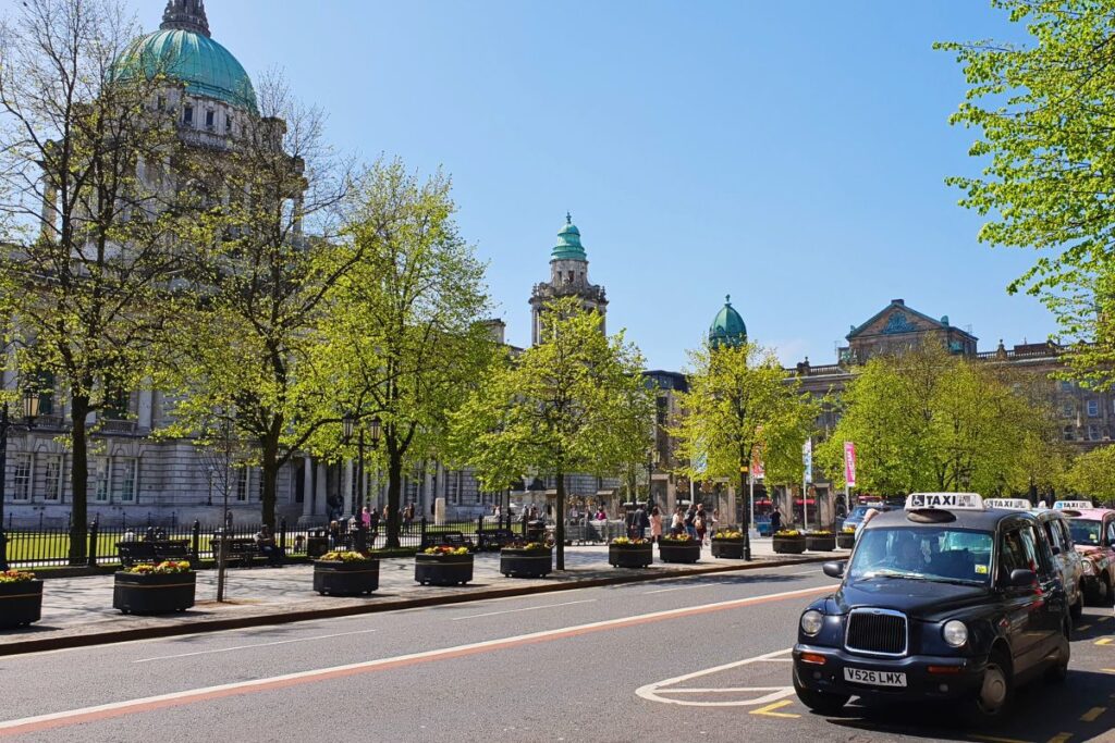 Das prächtige Rathaus (City Hall) von Belfast mit seiner grünen Kuppel, davor ein klassisches schwarzes Taxi auf der Straße.