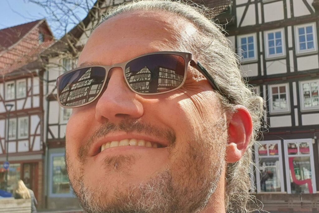 Nahaufnahme von Reiseblogger Nicolo Martin in Eschwege, in dessen Sonnenbrille sich die historischen Fachwerkhäuser spiegeln.