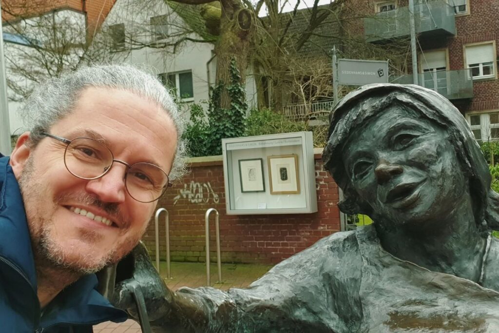 Reiseblogger Nicolo Martin macht lächelnd ein Selfie mit der Bronzestatue „Güths Mariechen“ in der Gütersloher Innenstadt.