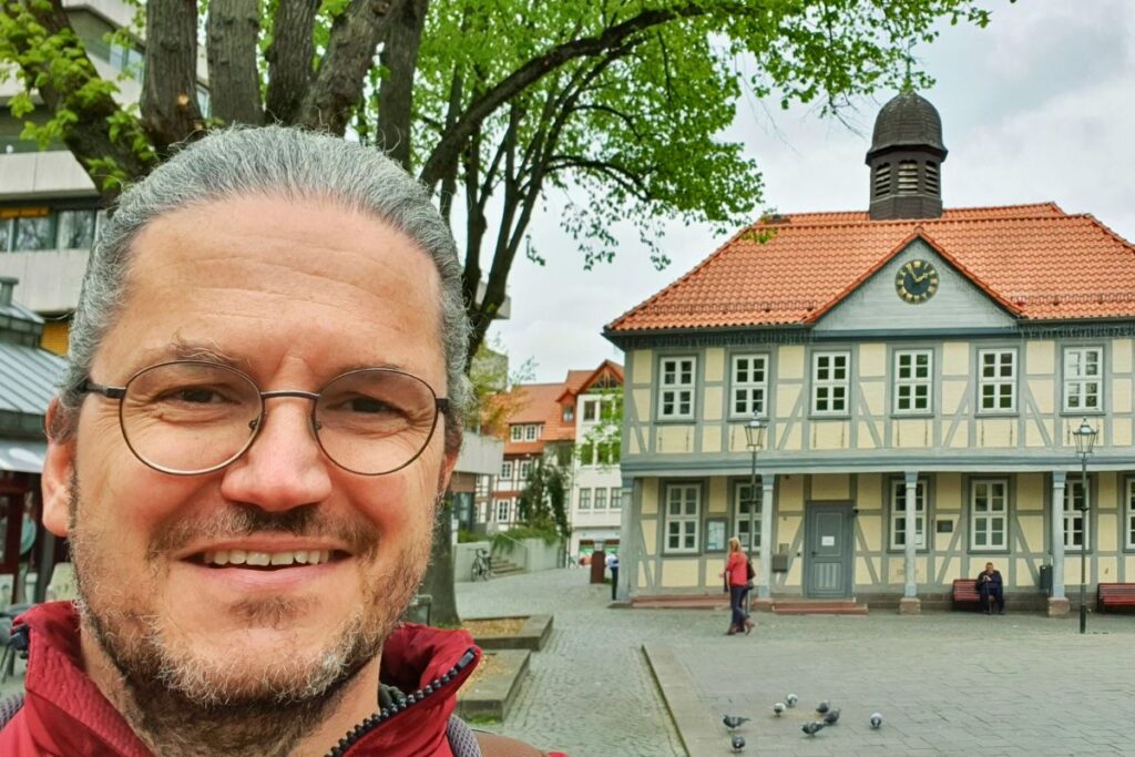 Reiseblogger Nicolo Martin lächelt vor einem historischen hellgelben Fachwerkgebäude in der Northeimer Altstadt.