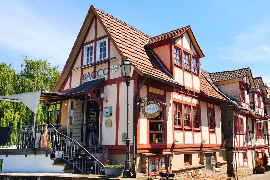 Die Fassade des Restaurants Bacco Esposito in einem historischen, beige-roten Fachwerkhaus mit einer Außentreppe und einer Terrasse in Rotenburg an der Fulda.