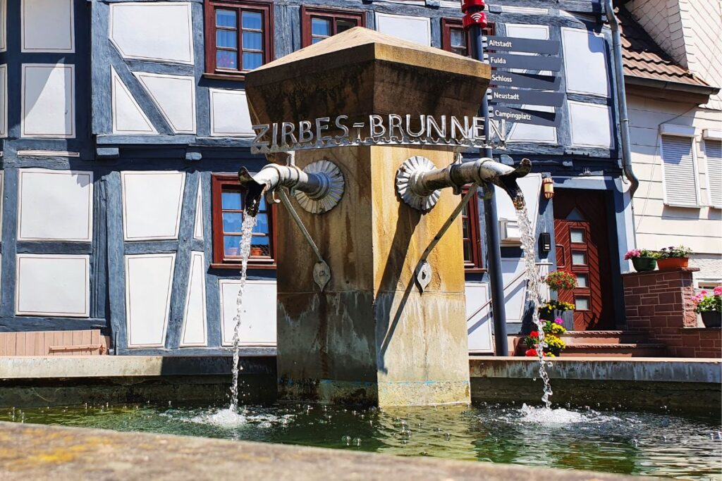 Der historische Zirbesbrunnen in Rotenburg an der Fulda mit zwei Wasserspeiern vor einer Kulisse aus traditionellen Fachwerkhäusern.