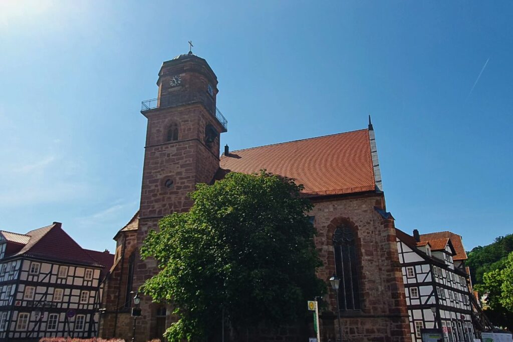 Die gotische Jakobikirche in Rotenburg an der Fulda aus rotem Sandstein, daneben historische Fachwerkbauten unter strahlend blauem Himmel.
