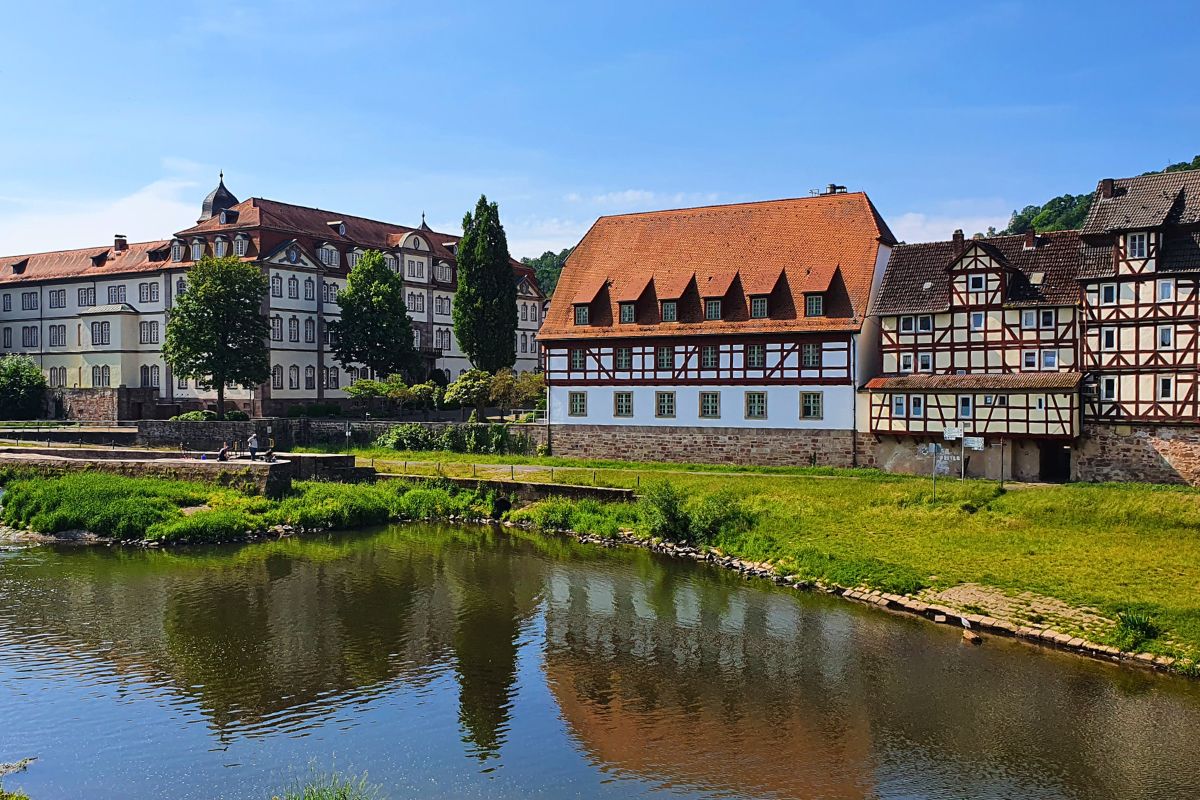 Blick über die Fulda auf das helle Landgrafenschloss und eine geschlossene Reihe bunter Fachwerkhäuser in Rotenburg.