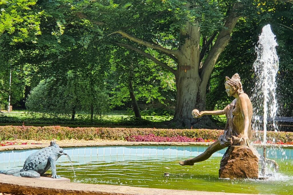 Bronzeskulptur des Froschkönigs und der Prinzessin an einem Springbrunnen im schattigen Schlossgarten von Rotenburg an der Fulda.