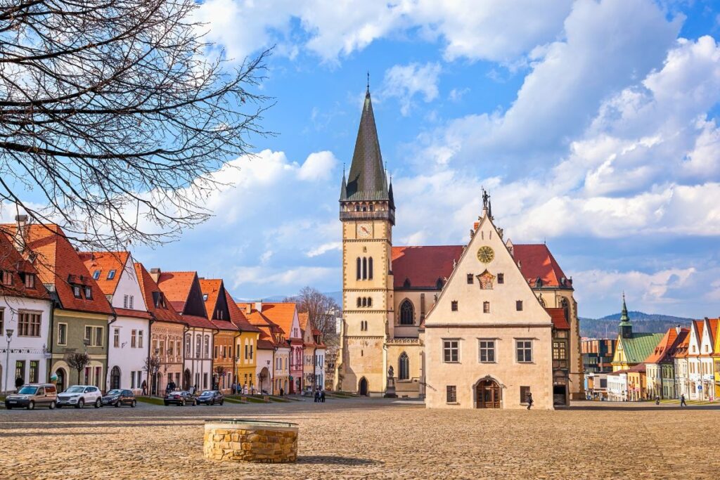 Der historische Marktplatz von Bardejov mit der St.-Ägidius-Basilika, dem alten Rathaus und bunten Giebelhäusern unter strahlend blauem Himmel.