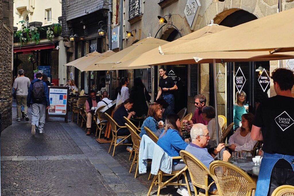 Eine enge, belebte Gasse im historischen Quartier du Bouffay in Nantes mit vielen Restaurantterrassen und Sonnenschirmen.