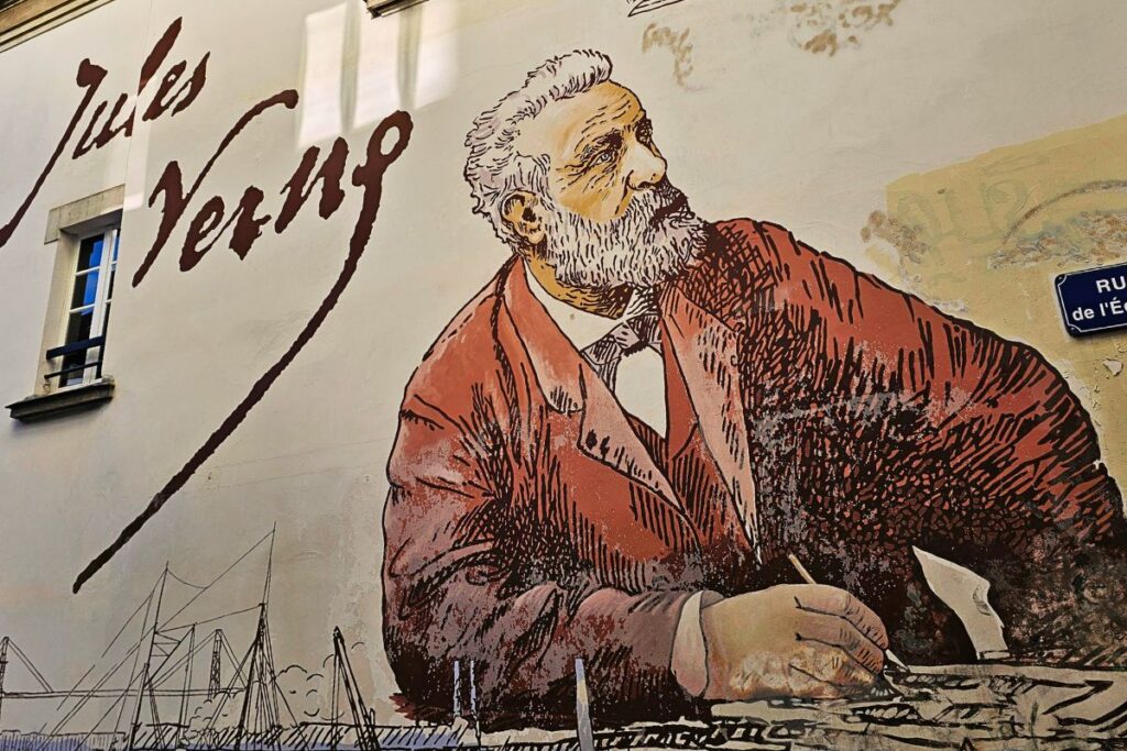 Ein riesiges, kunstvolles Wandgemälde in Nantes, das den Schriftsteller Jules Verne beim Schreiben zeigt, daneben ein Schriftzug seines Namens.