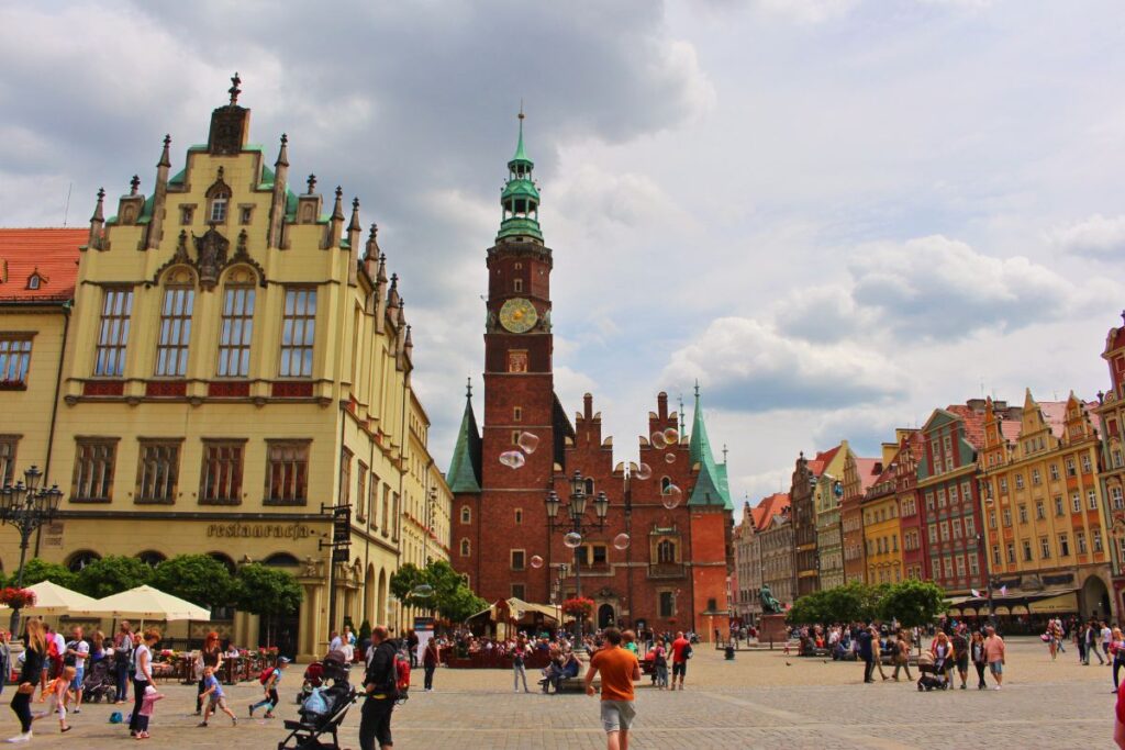 Der weitläufige Marktplatz in Breslau mit dem gotischen Alten Rathaus und einer Reihe farbenfroher Giebelhäuser unter einem weiten Wolkenhimmel.
