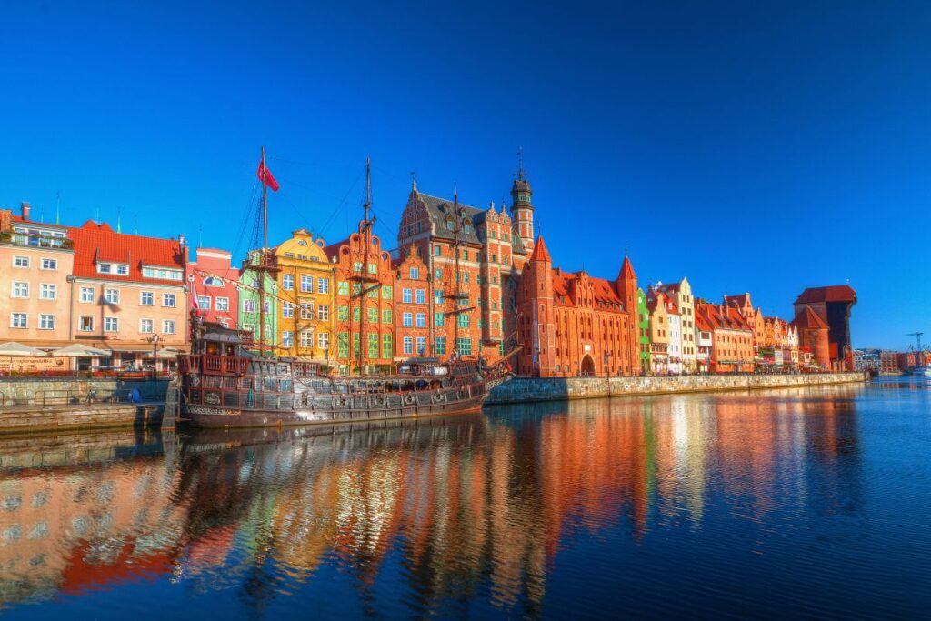 Die Uferpromenade von Danzig an der Motlau mit dem berühmten mittelalterlichen Krantor und prächtigen, farbigen Patrizierhäusern im hellen Sonnenlicht.