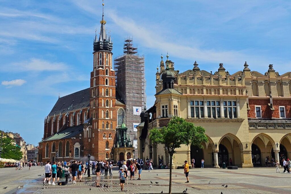 Der Hauptmarkt in Krakau mit den markanten Türmen der Marienkirche und den historischen Tuchhallen unter einem strahlend blauen Sommerhimmel.