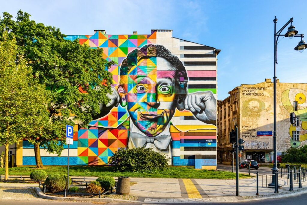 Ein riesiges, farbenfrohes Porträt-Mural des Pianisten Arthur Rubinstein an einer Häuserwand in Łódź, gestaltet in einem geometrischen Pixel-Stil.