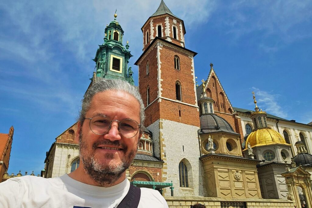 Reiseblogger Nicolo Martin lächelt vor der Wawel-Kathedrale in Krakau, im Hintergrund sieht man die markanten Türme und die glänzende goldene Kuppel der Sigismund-Kapelle.