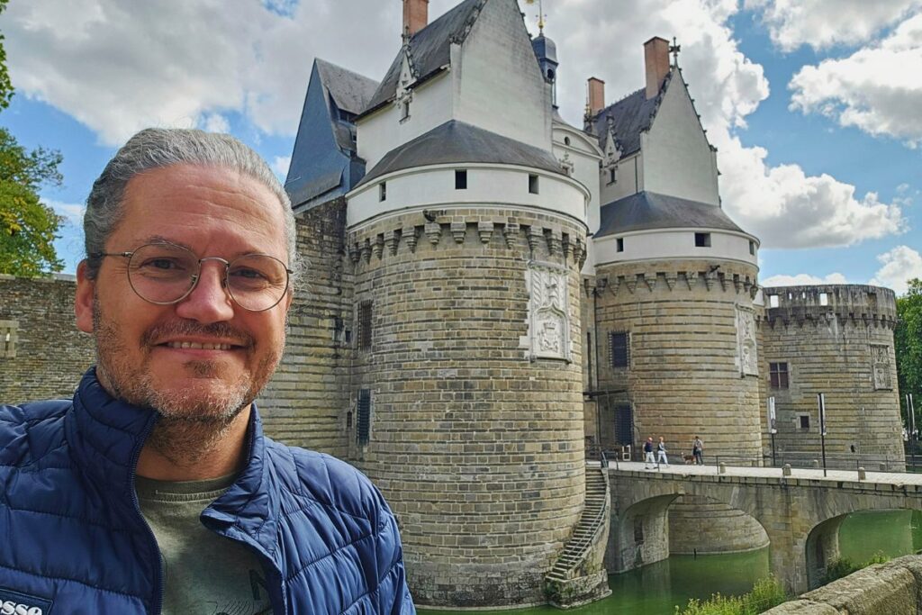 Reiseblogger Nicolo Martin lächelt vor den wehrhaften weißen Rundtürmen des Schlosses der Herzöge der Bretagne in Nantes.