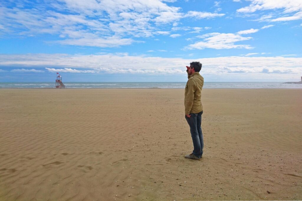 Reiseblogger Nicolo Martin steht auf dem weiten Sandstrand von Caorle und schaut sehnsüchtig auf das offene Meer hinaus.