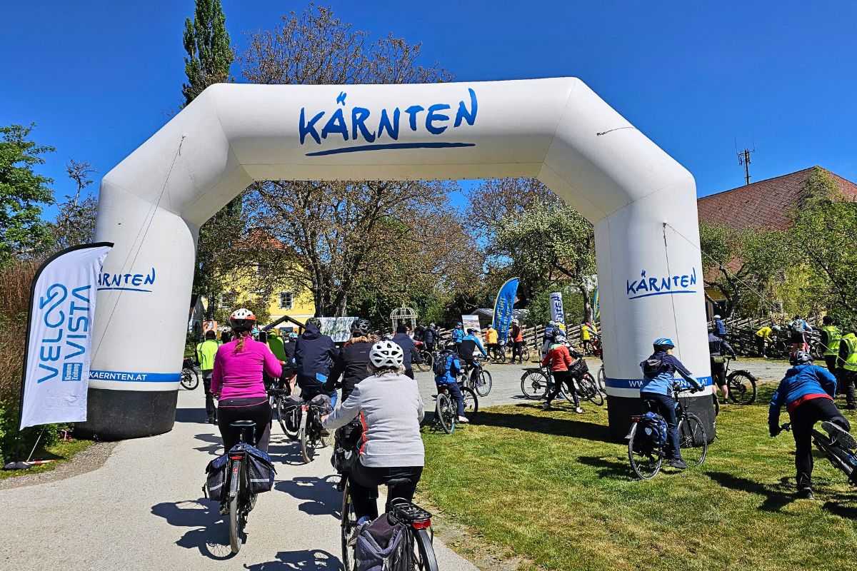 Radfahrer erreichen gut gelaunt die Buschenschenke Brunnerhof in Kärnten, wo im Garten gedeckte Tische für die kulinarische Stärkung bereitstehen.