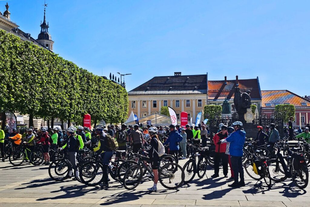 Eine Gruppe von Radfahrern und Radfahrerinnen versammelt sich auf dem Klagenfurter Neuer Platz für die Velovista-Radtour der Etappe 5.