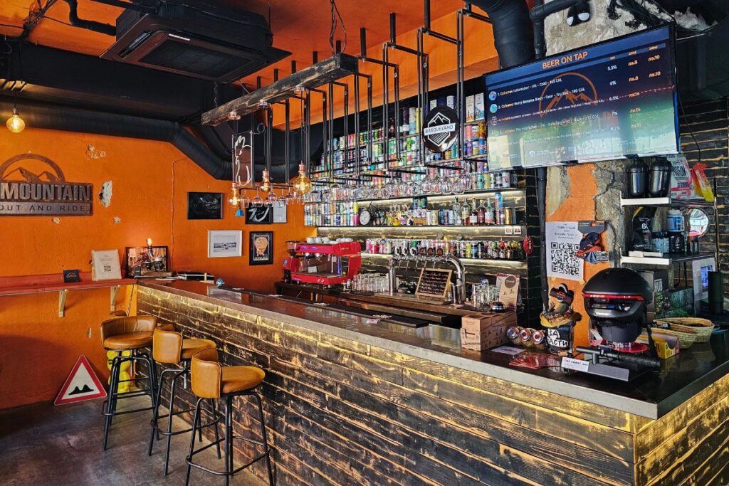 Die gemütliche, rustikale Holzbar im All Mountain Downtown Bike Shop in Sofia mit Barhockern und einer digitalen Tap-Liste an der Wand.