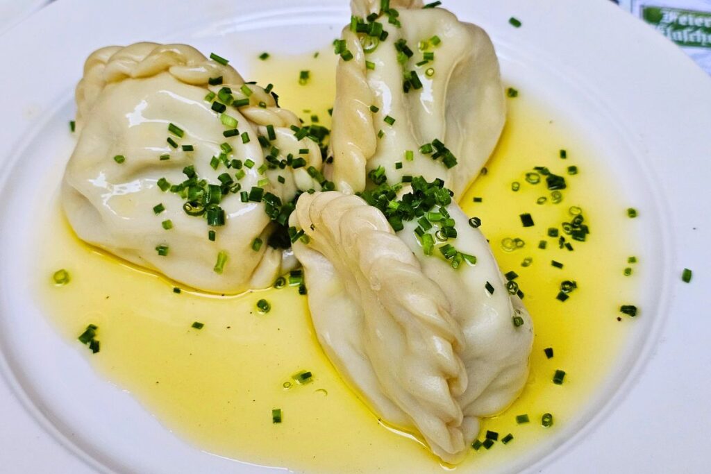 Drei traditionelle Kärntner Kasnudeln garniert mit frischem Schnittlauch in reichlich geschmolzener Butter auf einem weißen Teller im Bierhaus zum Augustin.