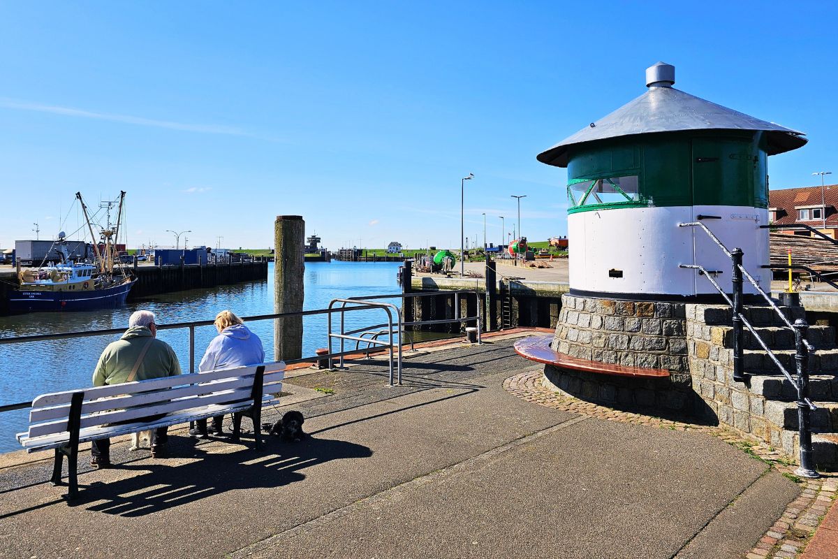Das kleinere grün-weiße Molenfeuer steht am Ende einer Steinmole direkt am Hafen in Büsum unter wolkenlosem Himmel.