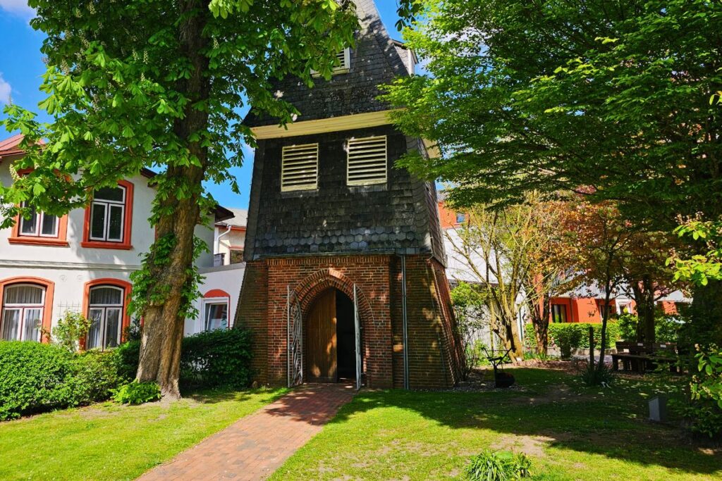 Der freistehende, historische Glockenturm neben der St. Clemens Kirche in Büsum vor blauem Himmel.