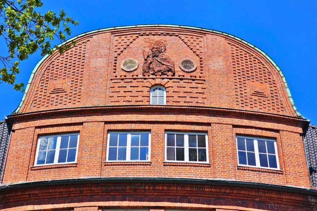 Die prächtige, halbrunde Backsteinfassade des Rathauses in Marne im neobarocken Stil mit einem kunstvollen Ziegel-Relief des Heiligen Matthäus im Giebel.
