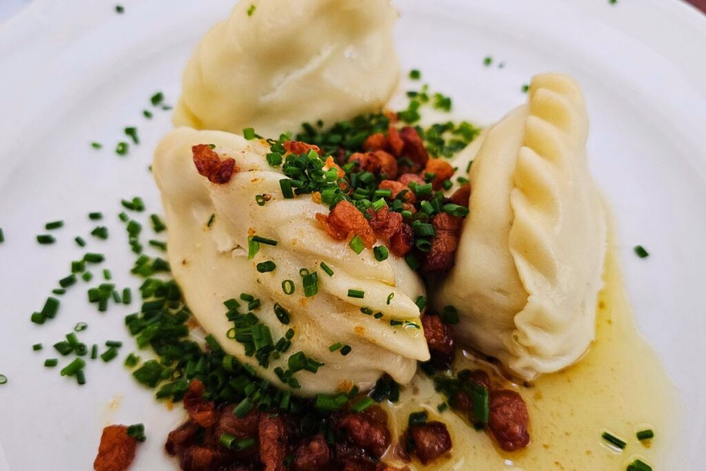 Drei Kärntner Kasnudeln garniert mit knusprigen Grammeln und viel Schnittlauch auf einem weißen Teller im traditionsreichen Gasthaus im Landhaushof.
