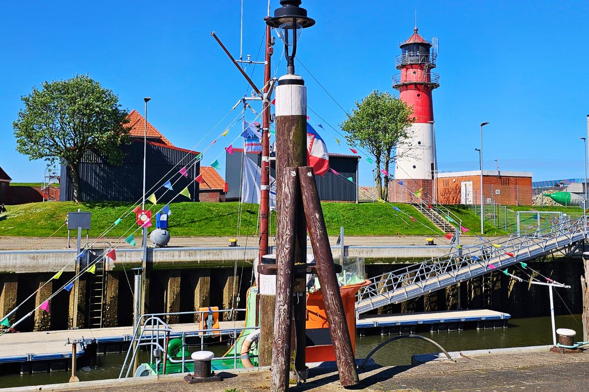 Der ikonische, rot-weiß gestreifte Leuchtturm von Büsum ragt hinter norddeutschen Dächern in den klaren blauen Himmel.