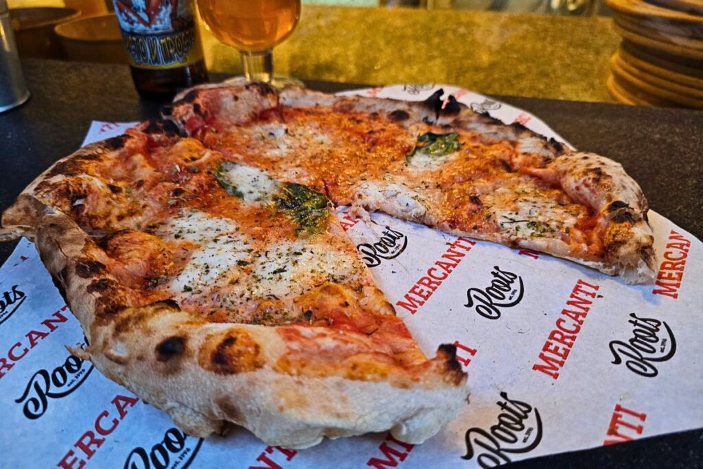 Eine frisch gebackene, neapolitanische Pizza Margherita auf bedrucktem Papier auf einem Bartresen in Sofia, im Hintergrund eine Flasche Craft Beer.