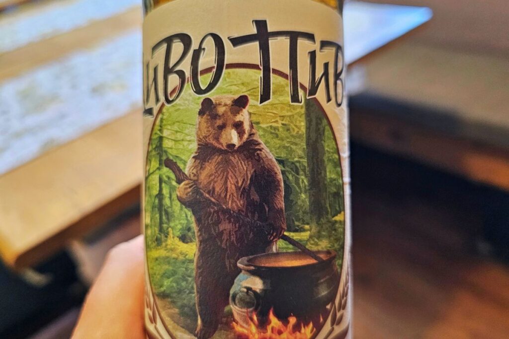Nahaufnahme des Etiketts einer "Divo Pivo"-Bierflasche mit einem braunen Bären, der einen Kochtopf über einem offenen Feuer rührt.