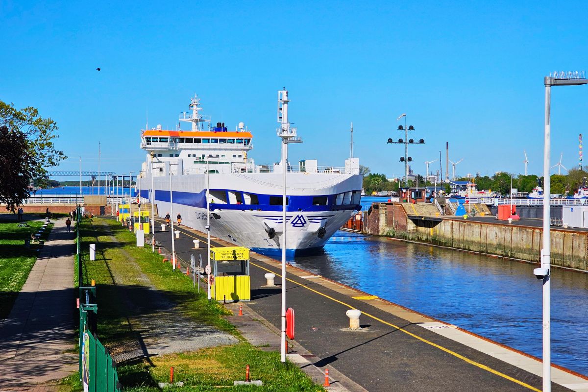 Ein großes weiß-blaues Frachtschiff passiert die gewaltige Schleusenanlage des Nord-Ostsee-Kanals in Brunsbüttel unter strahlend blauem Himmel.