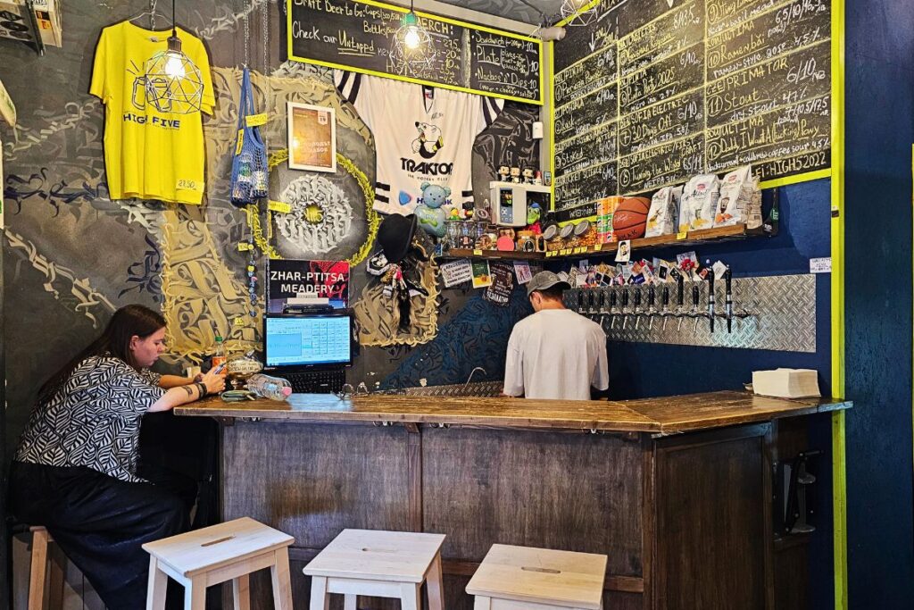 Die gemütliche Holztheke im High Five Taproom in Sofia mit einer detaillierten Kreidetafel-Speisekarte und einem Barkeeper von hinten.