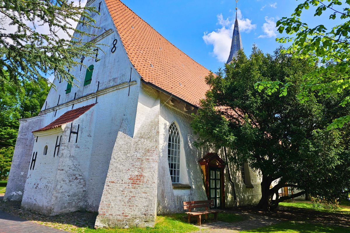 Die ehrwürdige Fischerkirche St. Clemens in Büsum mit weiß getünchten Backsteinen und mit hellen Fenstern im hellen Sonnenlicht.