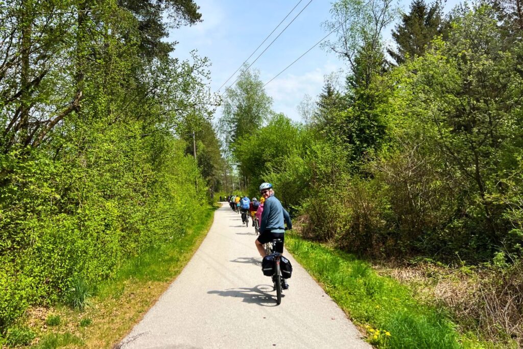 Nicolo Martin befährt einen flachen, asphaltierten Radweg inmitten von dichten grünen Hürden und blickt gut gelaunt zurück über die Schulter.