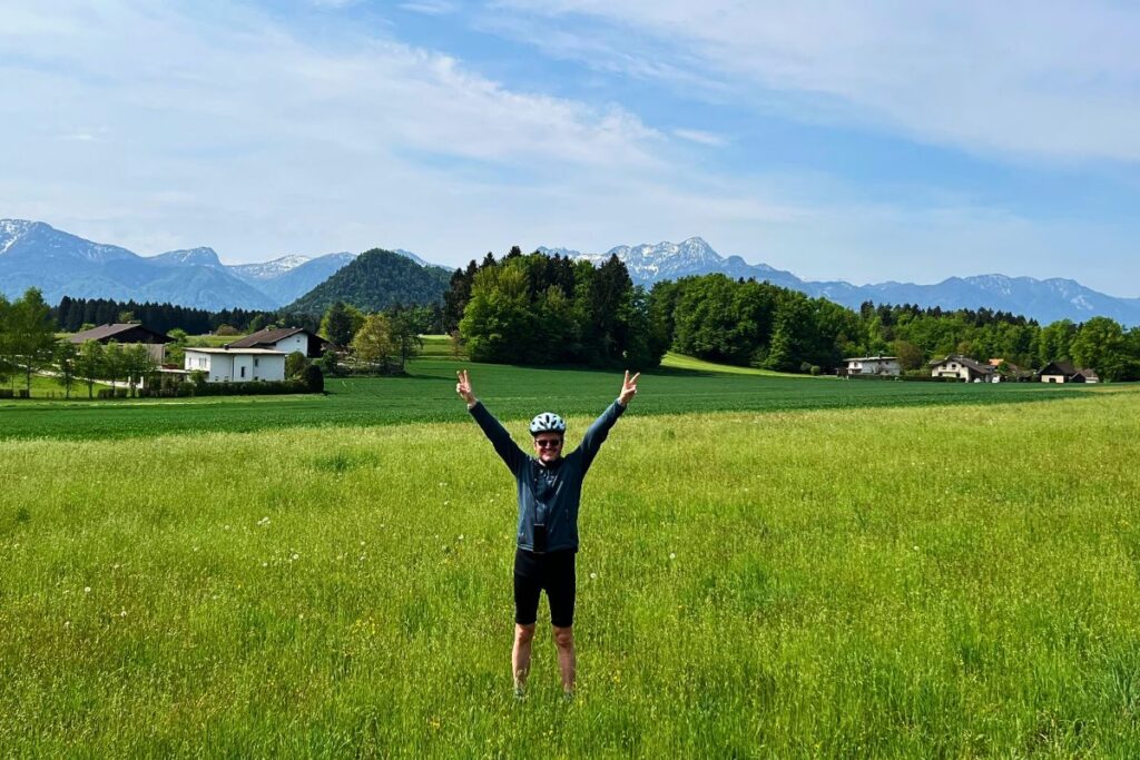 Nicolo Martin steht mit jubelnd ausgestreckten Armen in einer riesigen grünen Wiese vor dem Panorama des markanten Berges Mittagskogel.