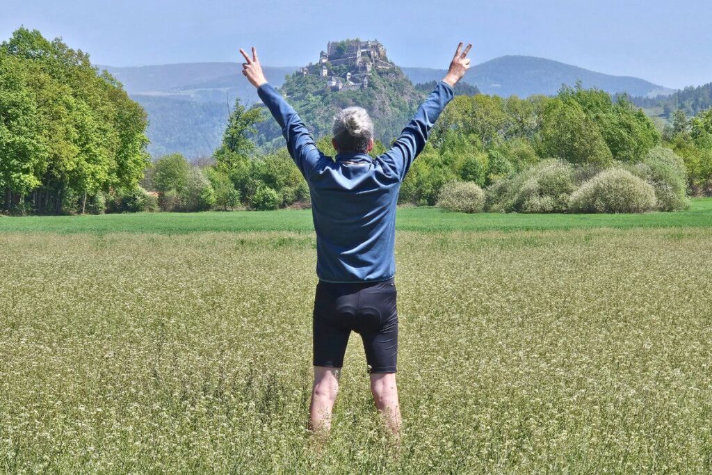Reiseblogger Nicolo Martin steht von hinten zu sehen mit erhobenen Armen und Victory-Zeichen in einer Blumenwiese vor der Kulisse der Burg Hochosterwitz.