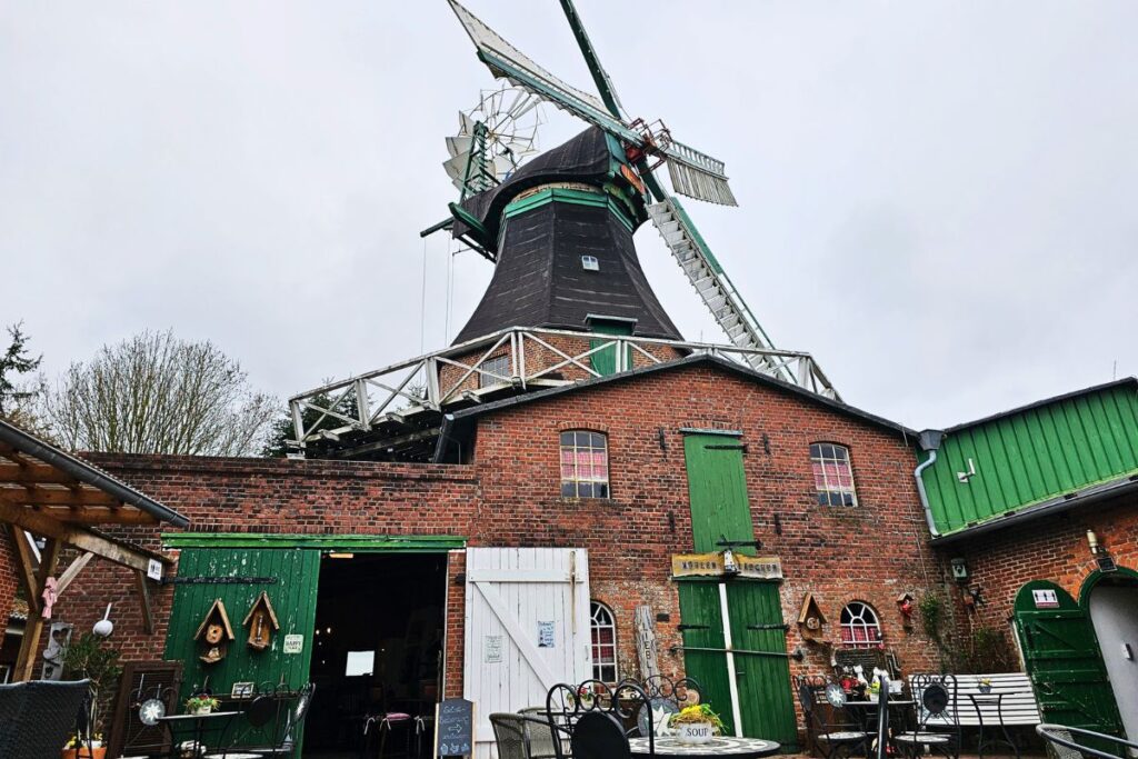 Eine historische Windmühle aus rotem Backstein und dunklem Holz in Barlt, die heute als gemütliches Café mit einer einladenden Außenterrasse genutzt wird.