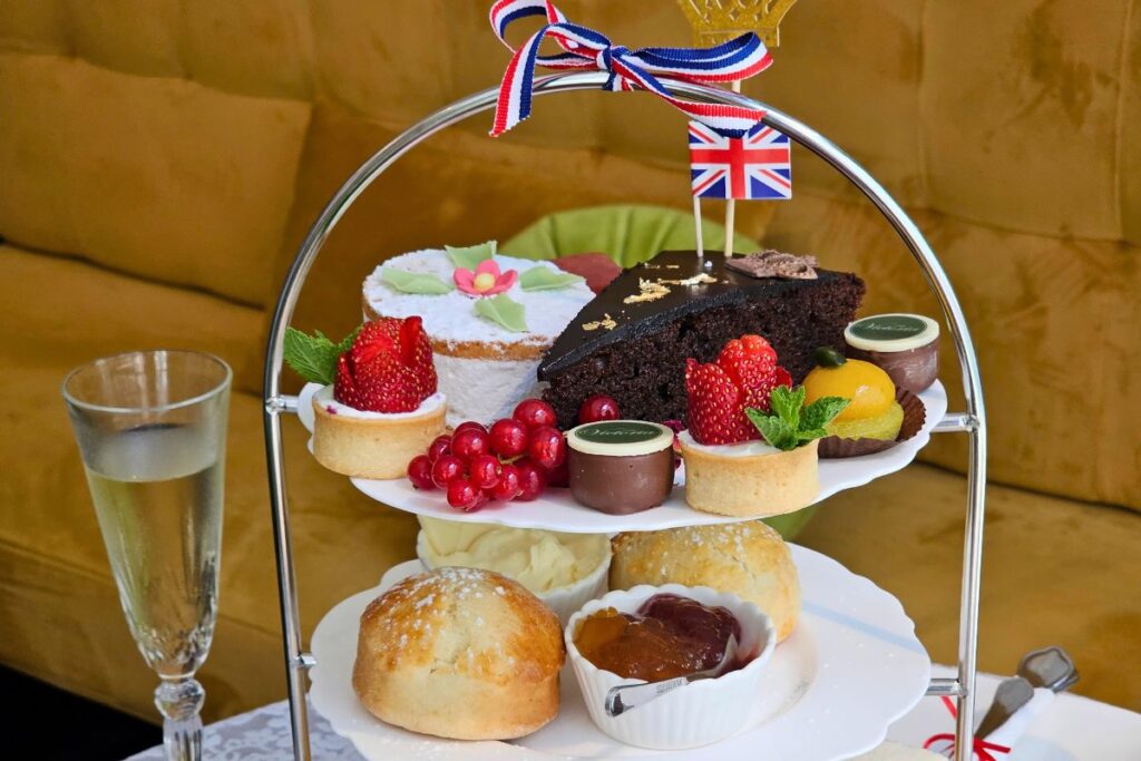 Eine zweistöckige silberne Etagere reich beladen mit Scones, frischen Erdbeer-Törtchen, Schokoladenkuchen mit Blattgold und einer kleinen britischen Flagge im Café Victoria in Coburg.